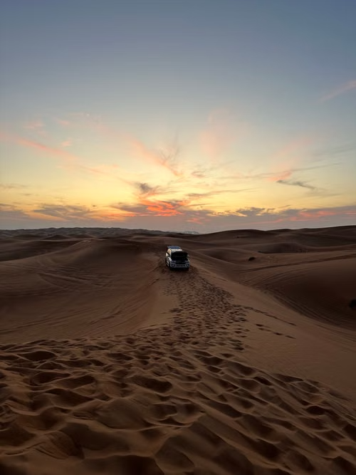 4×4 support vehicle crossing Sahara dunes at sunset